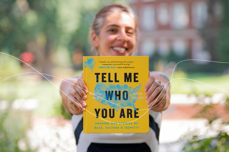A woman holding out a book titled "Tell Me Who You Are".