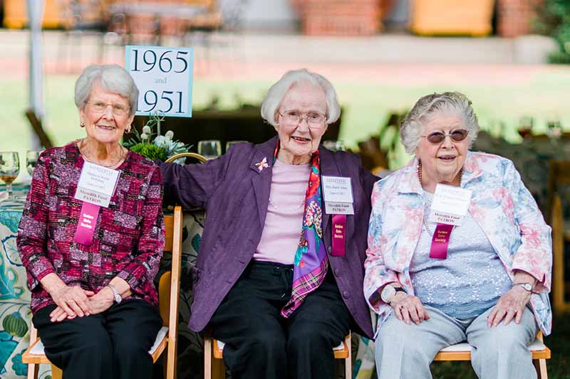 Three older women sit by each other smiling.