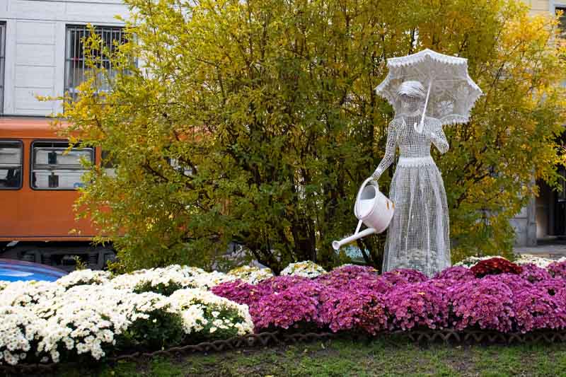 A sculpture of a woman watering over a real flowerbed.