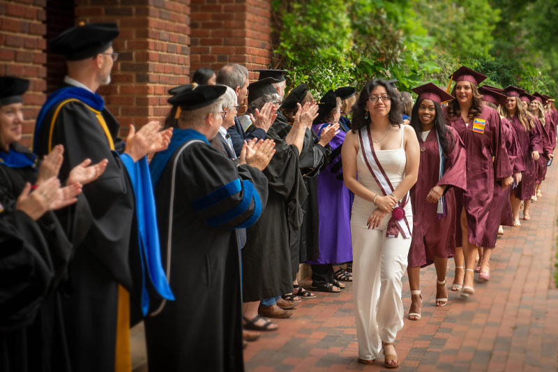 An usher leads the graduates through a lineup of faculty.
