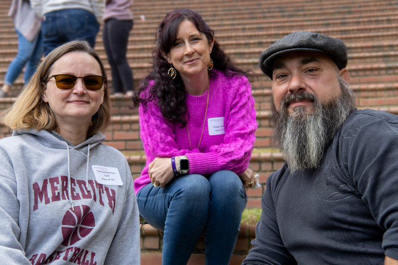 Three people smile at the camera, including two alumnae.