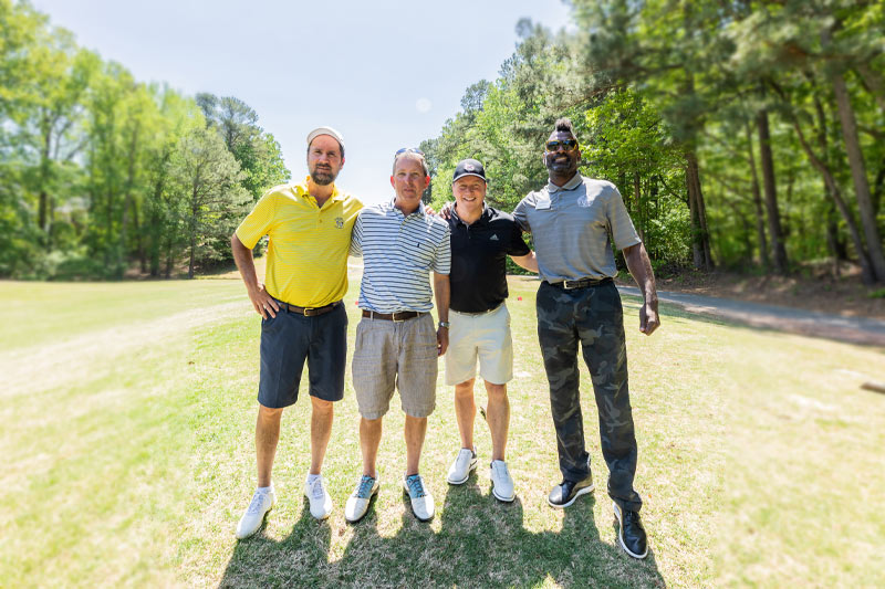 Four people pose for a photo on the course with their golf clubs.
