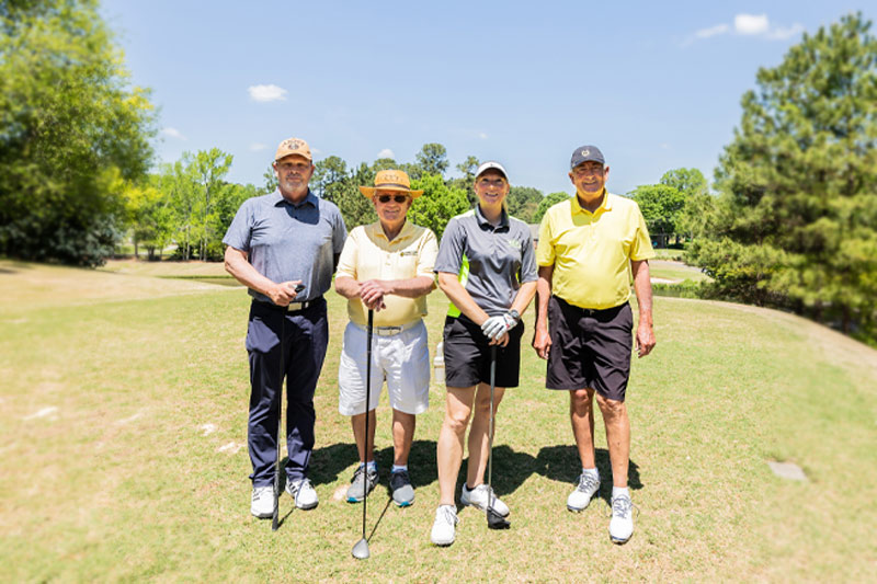 Four people pose for a photo on the range with their golf clubs.