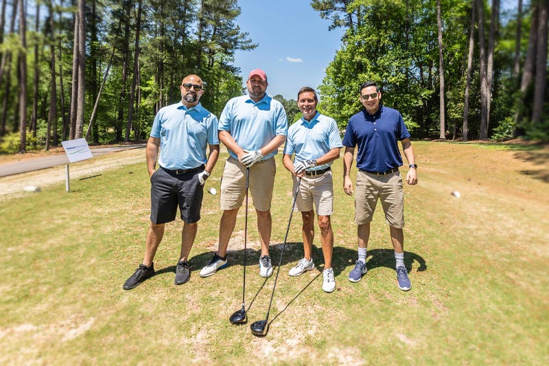 Four people pose for a picture on the range with their clubs.