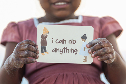 A dark skinned child holding a sign that says "I can do anything".