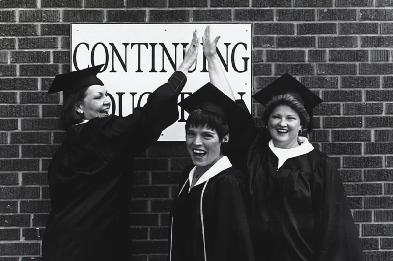 Wings graduates pose with a "continuing education" sign after graduation.