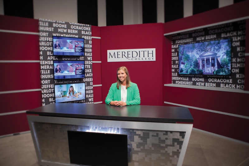 A student sitting at the anchor desk in the new media area.