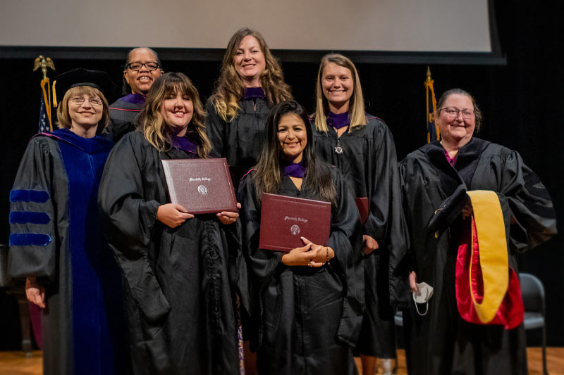 Masters in Criminal Justice graduates pose with their diplomas and professors at their graduation.