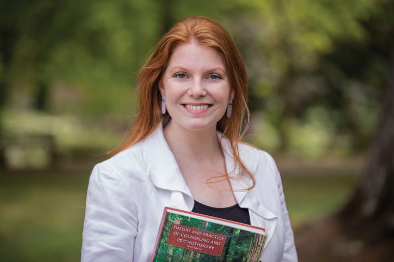 Veronica Harrison smiling and holding a "Theory and Practice of Counseling and Psychotherapy" book.