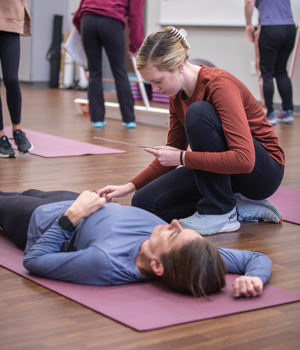 A student works with a patient on a yoga mat. 