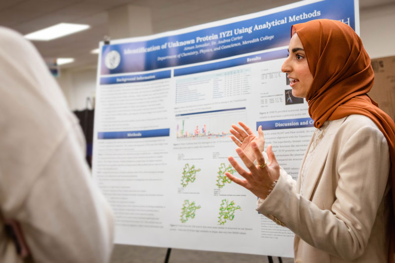 A student in a hijab presents her poster on CSA day.