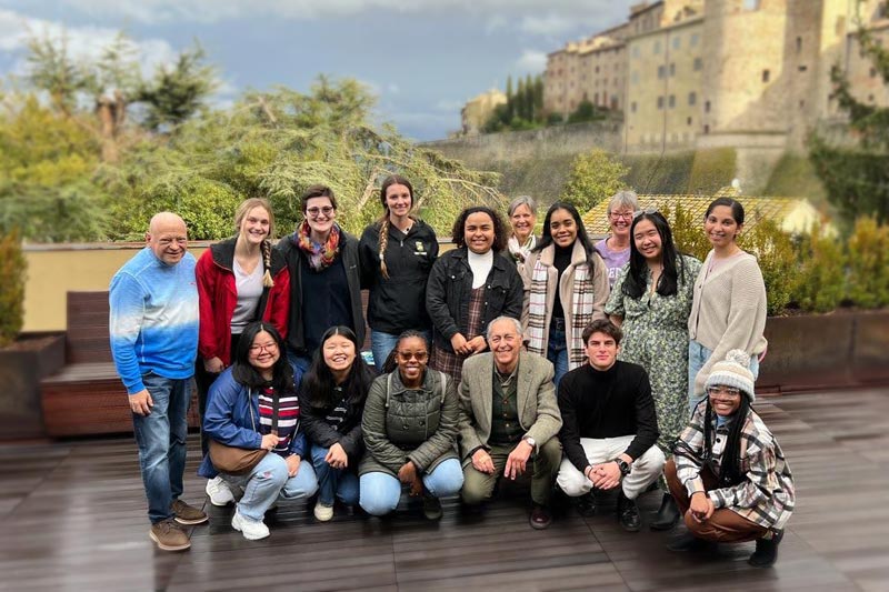 Students in a group in front of beautiful Italian greenery and buildings.