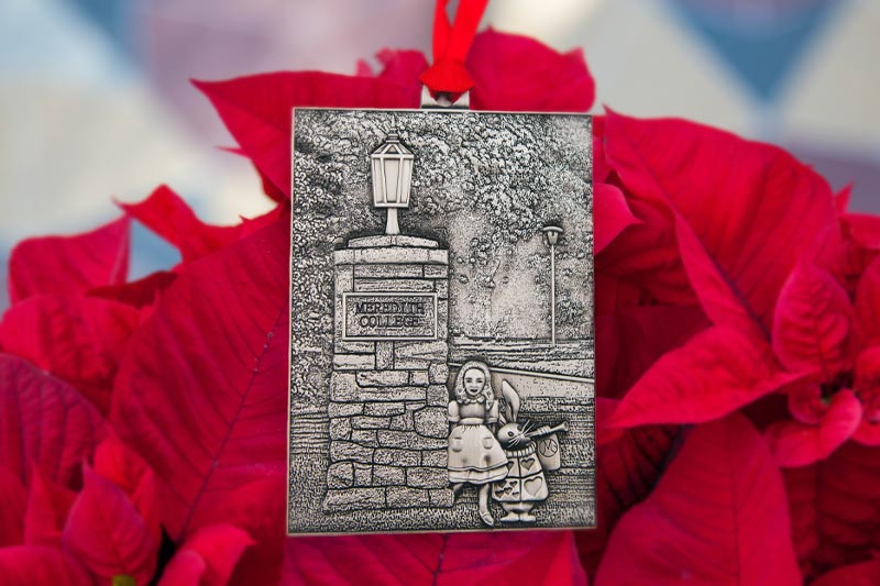 The 2023 pewter ornament showing a column with meredith college on it and Alice and the White Rabbit from Alice in Wonderland.
