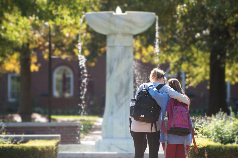 Two students hugging in front of the Meredith fountain.