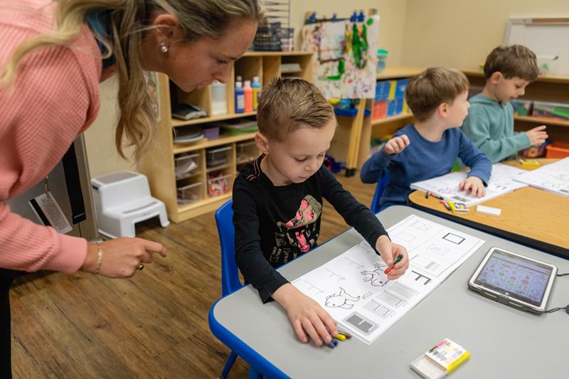 A teacher looks over the shoulder of her preschoolers in the Meredith Autism Program.